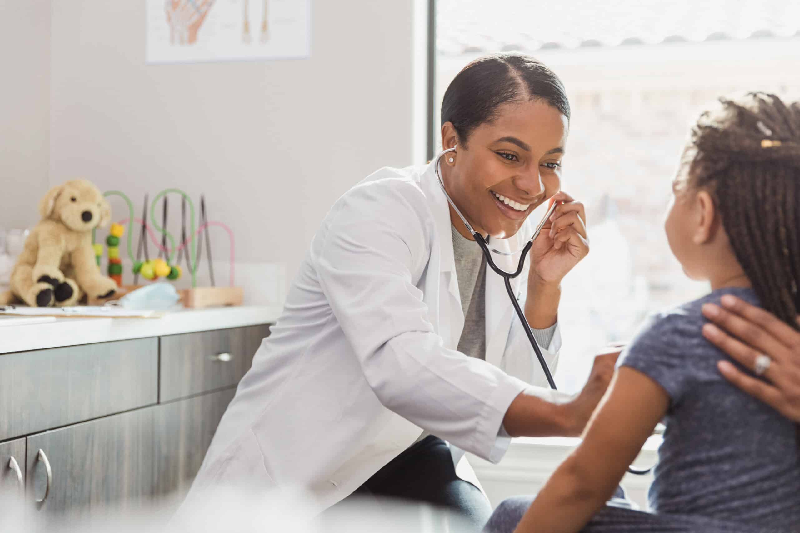 The mid adult female pediatrician smiles as she uses her stethoscope to listen to the little girl's heart.